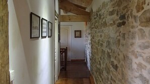 A narrow hallway with wooden beams and stone walls, leading to a door at the end.
