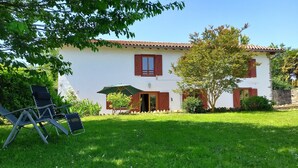 A white building with red shutters, a green umbrella, and a tree in the yard.