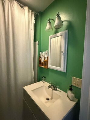 A bathroom with a white sink, green walls, a white door, and a shower curtain.