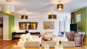 Ein modernes Wohnzimmer mit einer Couch, einem Esstisch mit Weinglas und Weinflasche sowie einem Fernseher.