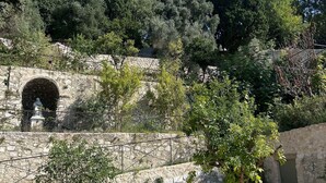Ein gepflasterter Weg führt zu einer Steinmauer mit einem Rundbogen.