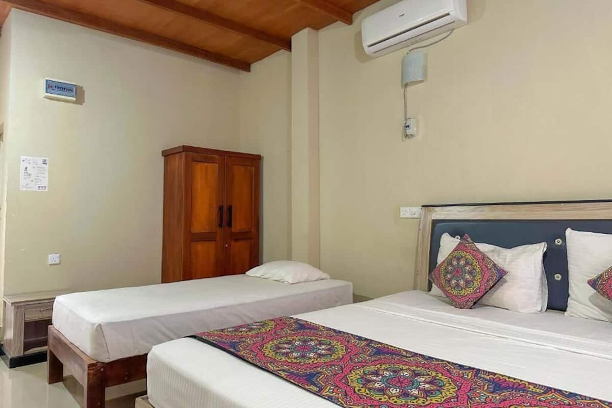 A room with two beds, a wooden wardrobe, an air conditioning unit, and a ceiling with wooden beams.