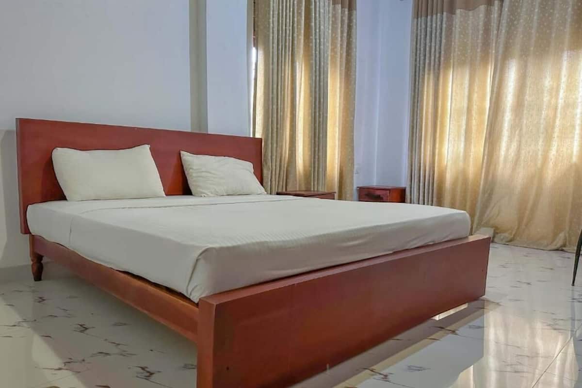 A bed with a wooden frame and white bedding in a room with a tiled floor and curtains.