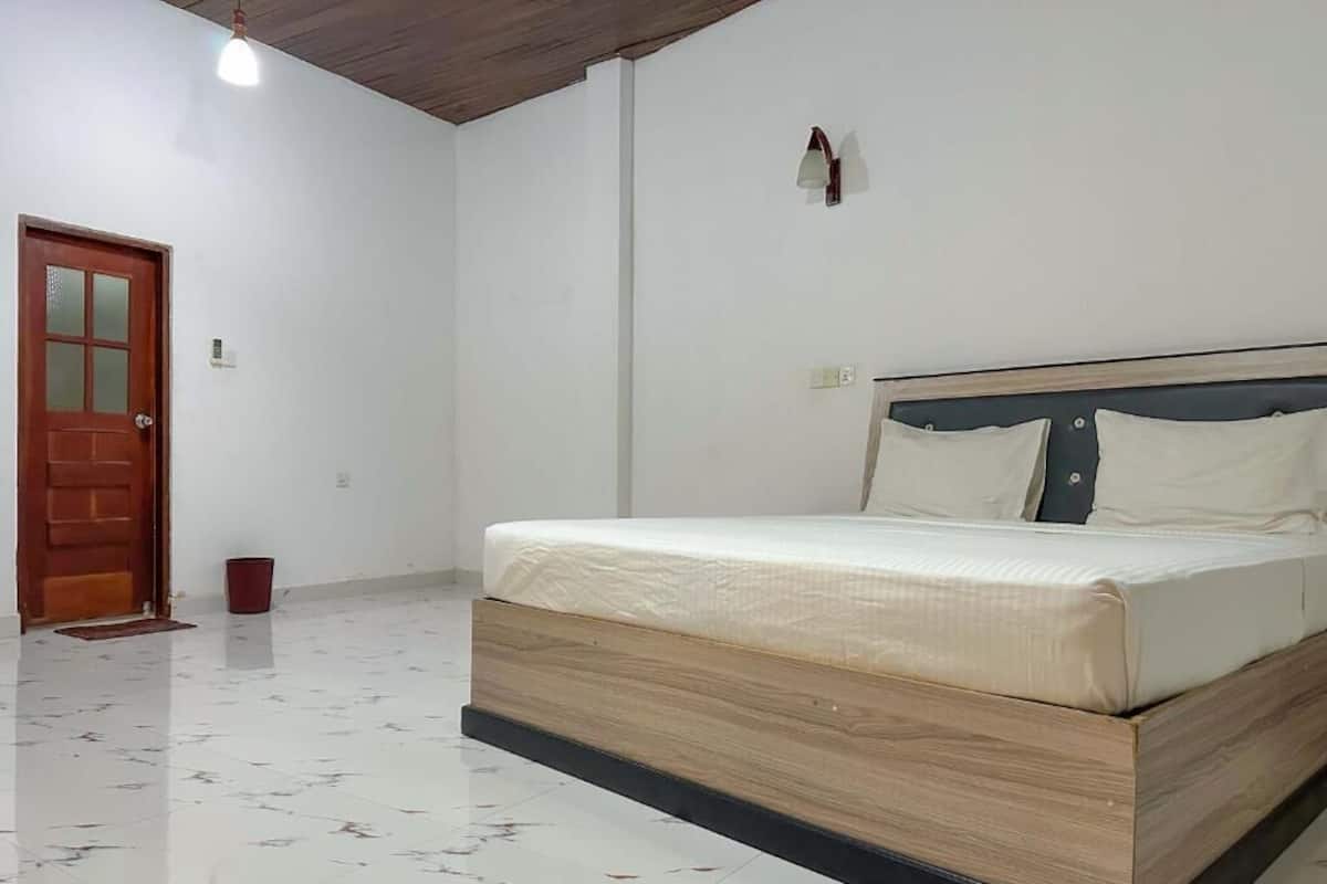 A bedroom with a wooden bed frame, white bedding, a red door, and a tiled floor.