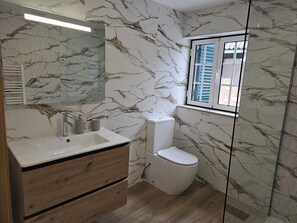 A bathroom with marble walls, a wooden vanity, a white sink, a toilet, and a window with shutters. - Destro village (Lindoso)