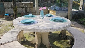 A round outdoor table with a white speckled surface, surrounded by a low stone wall. - Destro village  (Lindoso)