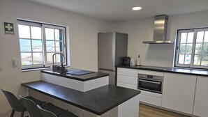 A modern kitchen with a central island, two bar stools, a built-in oven, and a stainless steel refrigerator. - Destro village  (Lindoso)