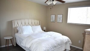 A bedroom with a tufted headboard, a single bed, a nightstand, a small round stool, and a ceiling fan.
