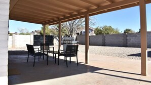 An outdoor patio with a grill, chairs, and a concrete floor.