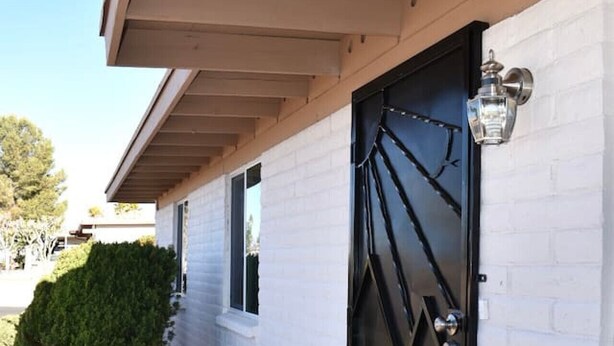 A white building with a black door, a small window, and a metal lantern on the wall.