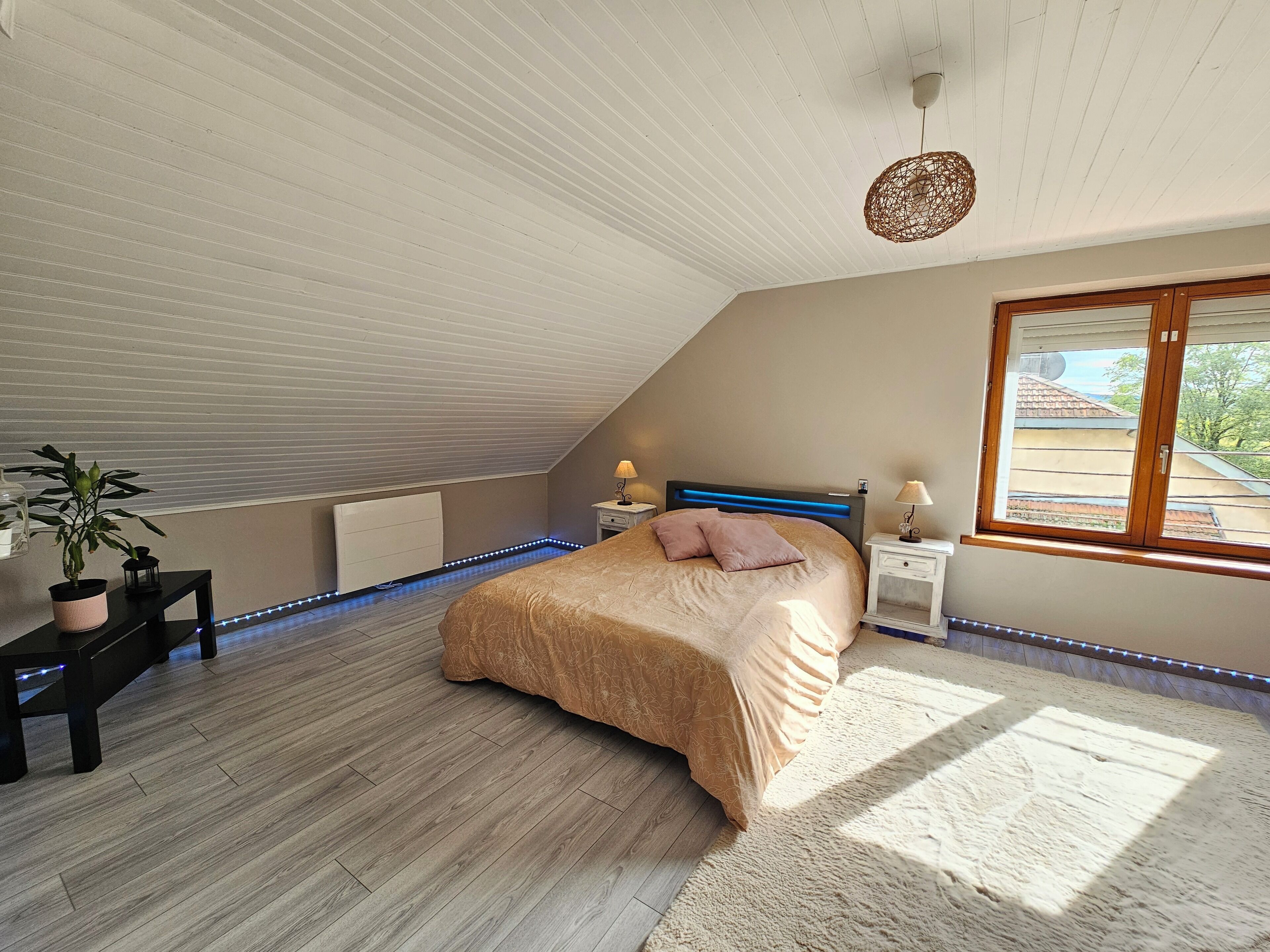 Une chambre avec un plafond en pente, un lit avec une tête de lit, des tables de chevet, une fenêtre et un radiateur.