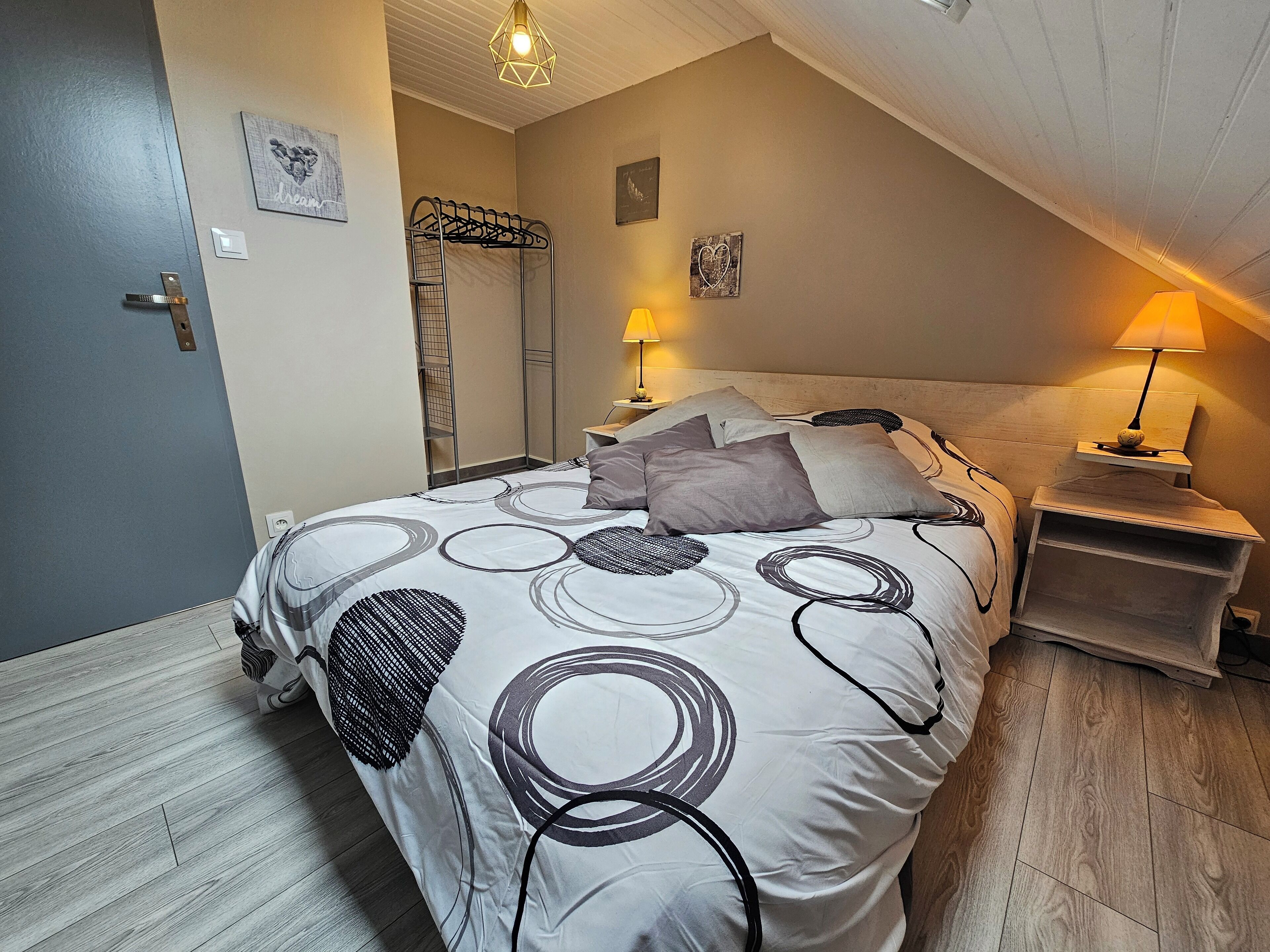 A bedroom with a bed, two bedside lamps, a wooden nightstand, and a wall-mounted coat rack.