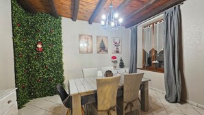 Un espace repas doté d’un plafond en bois, d’un lustre, d’un mur vert agrémenté de décorations et d’une fenêtre avec des rideaux.
