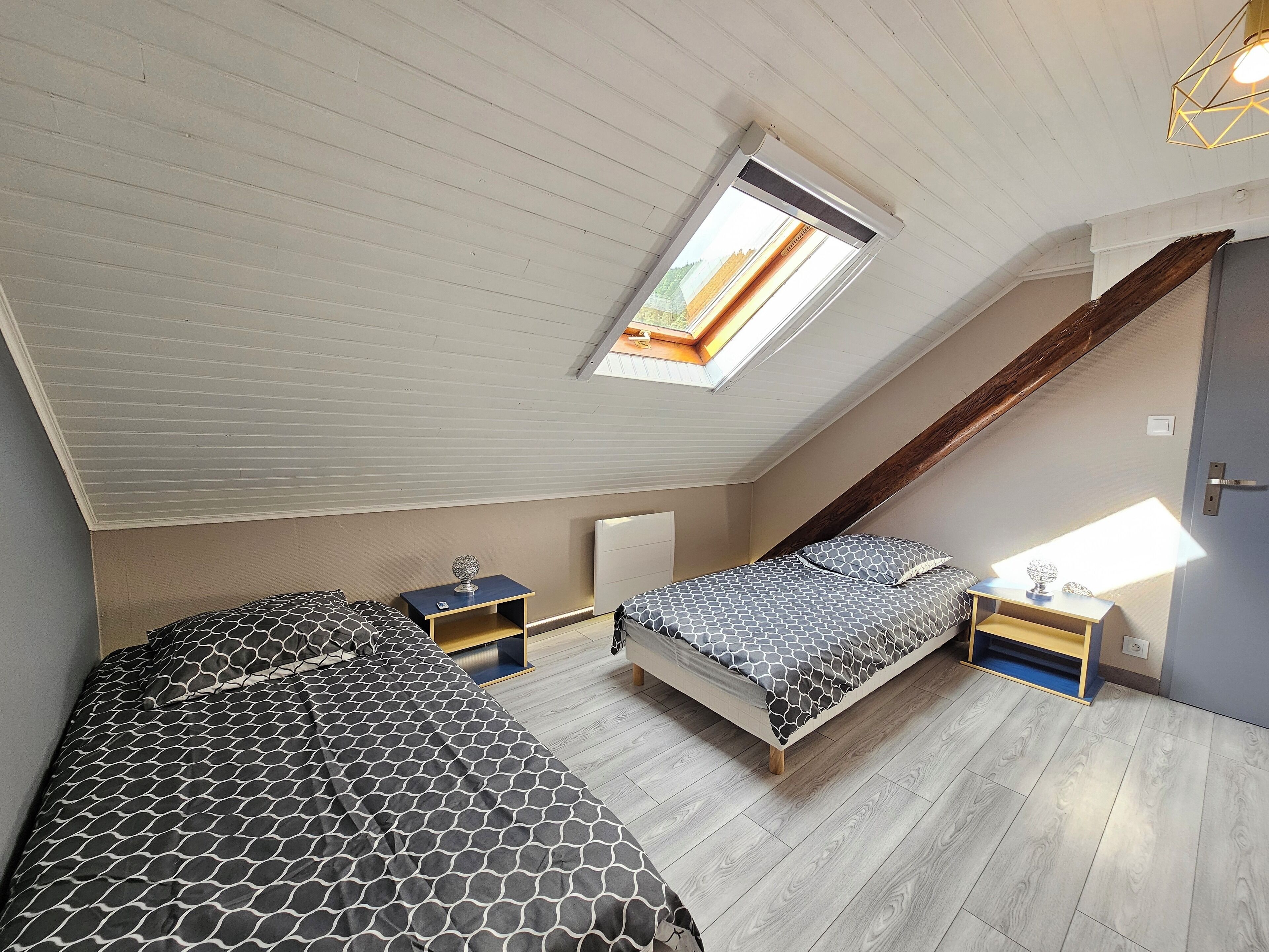 Une chambre avec deux lits, une lucarne, des poutres en bois et un plafond en pente.