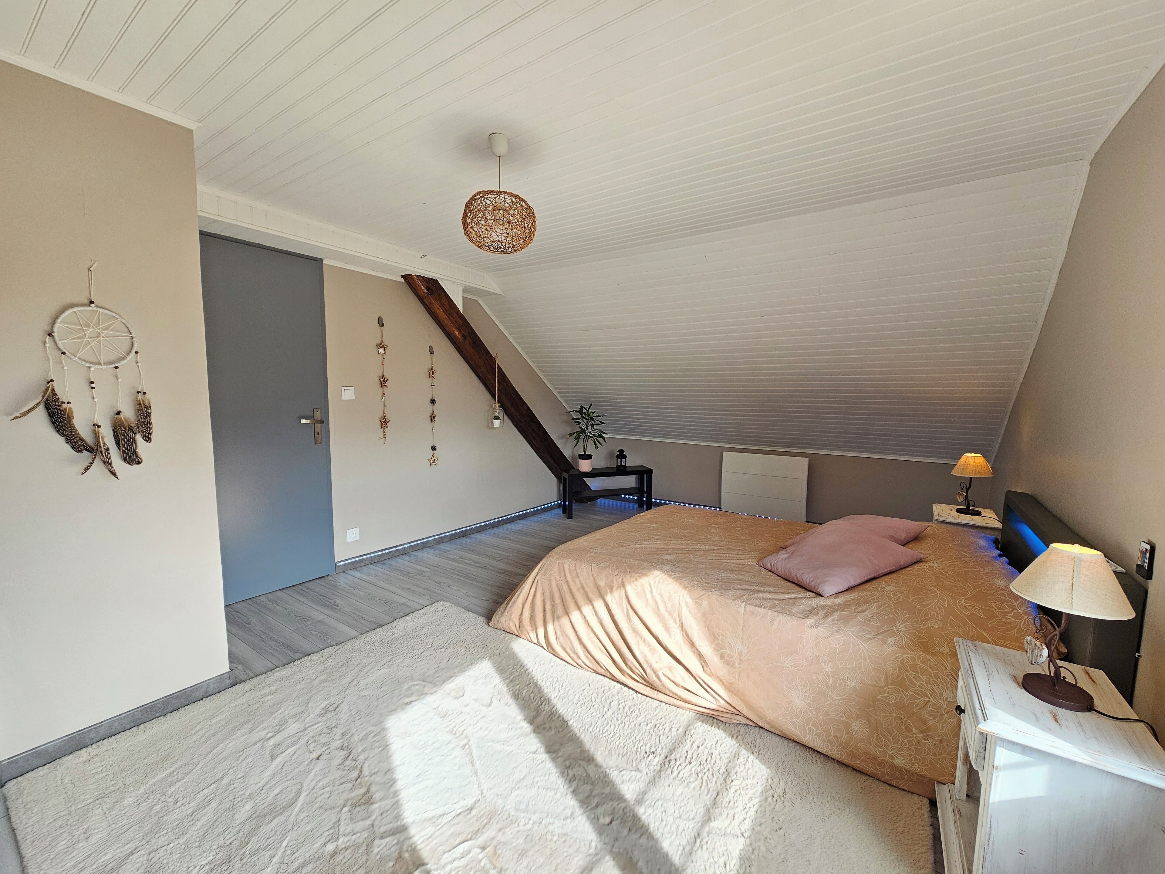 Een slaapkamer met een groot bed, een nachtkastje, een lamp, een dromenvanger en een trap.