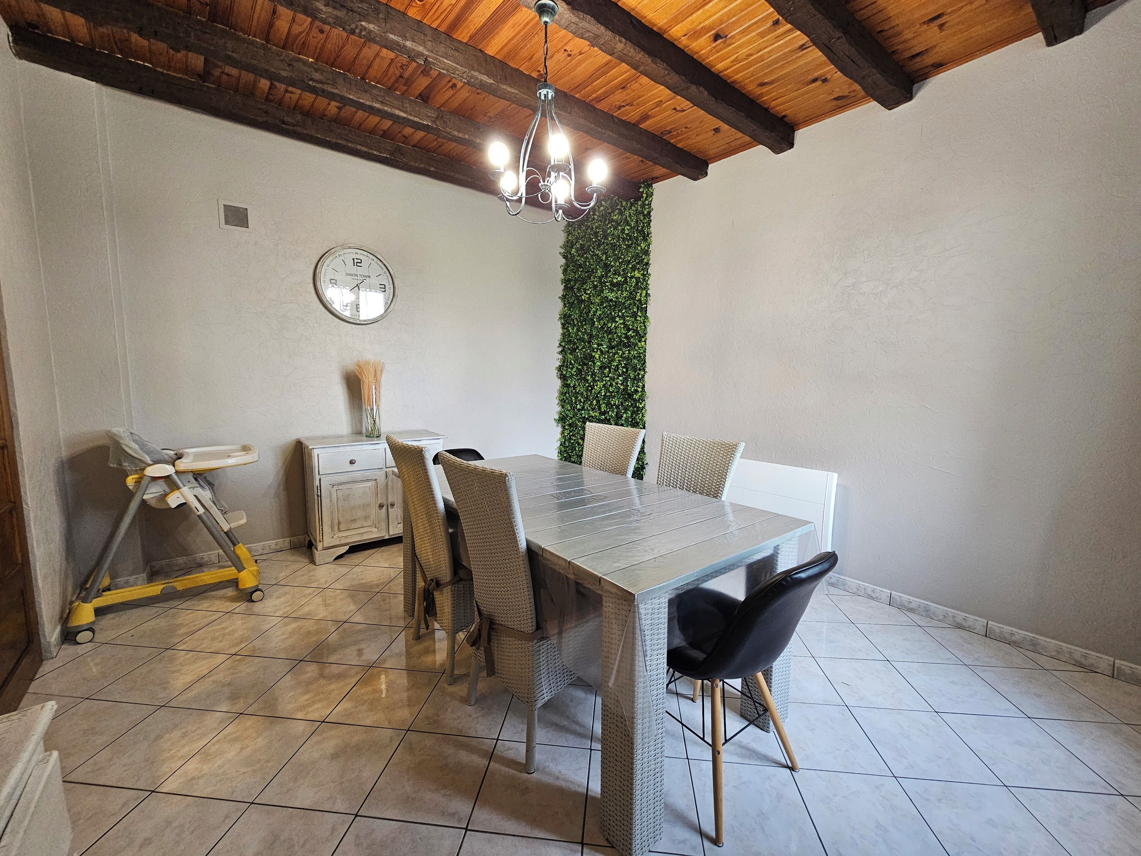 A dining area with a wooden ceiling, a clock on the wall, a green wall, and a tiled floor.
