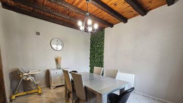 A dining area with a wooden ceiling, a clock on the wall, a green wall, and a tiled floor.