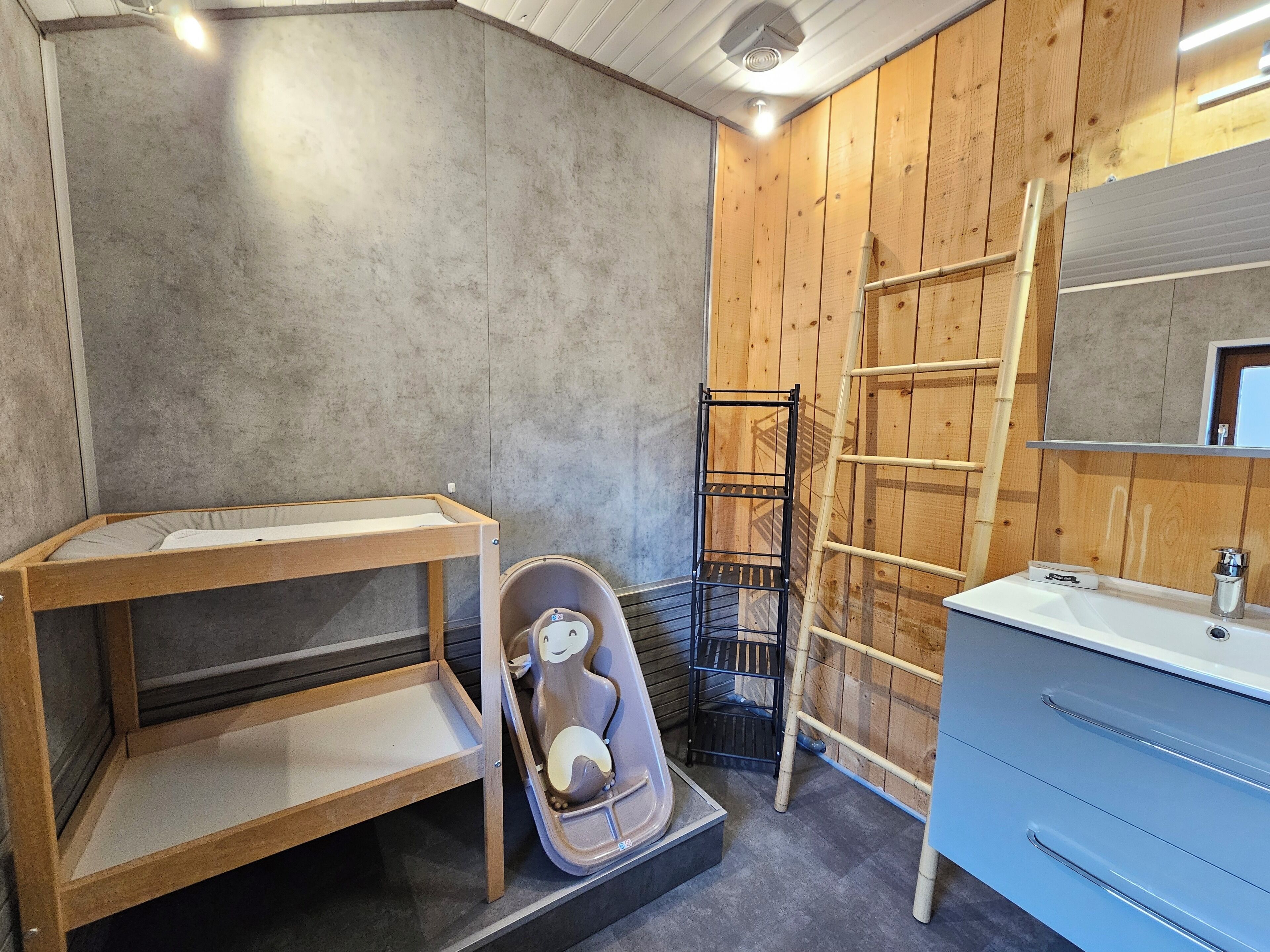 A bathroom with a wooden vanity, a small shelf, a toilet, and a ladder.