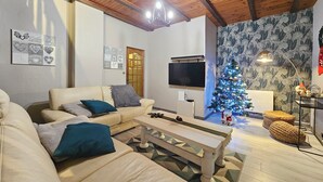 Un salon avec un plafond en bois, un canapé beige, une table basse, un téléviseur, un sapin de Noël et un papier peint à motifs.