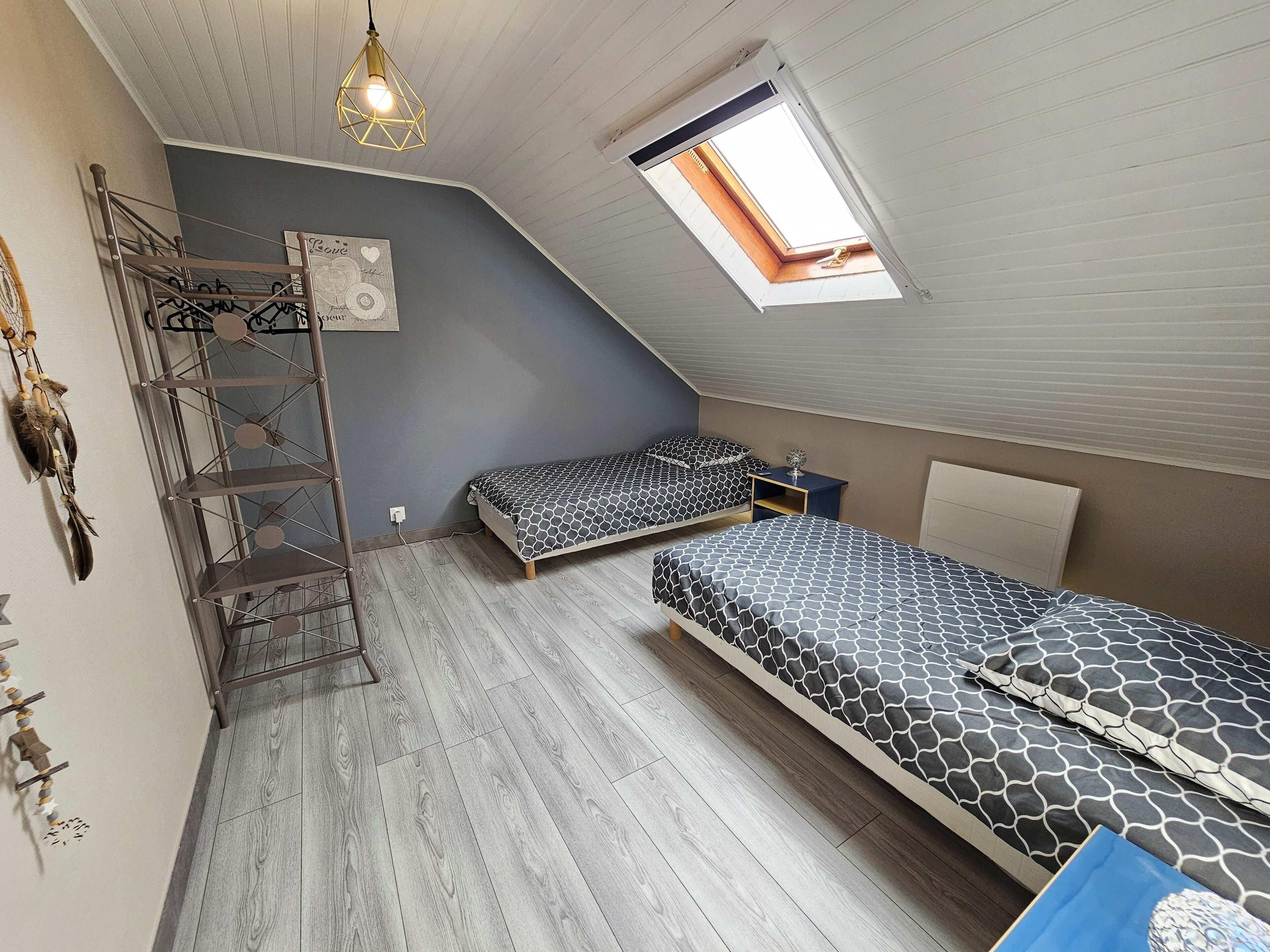 Ein Schlafzimmer mit zwei Betten, einem Oberlicht, einer Hängeleuchte und einem Wandregal.