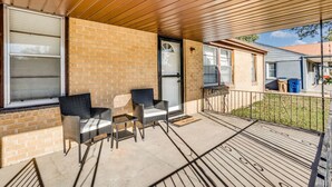A covered porch with two wicker chairs and a small table, a brick wall, and a sliding glass door. - •new• Grace’s Getaway - sleeps 6 (Derby)