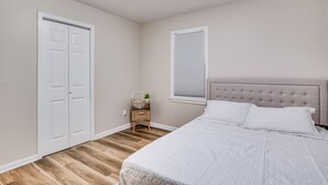 A bedroom with a bed, a nightstand, a window with blinds, and a door. - •new• Grace’s Getaway - sleeps 6 (Derby)