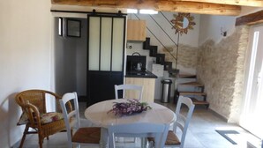 Un comedor con una mesa redonda y sillas, una cocina al fondo y una escalera que sube a otro nivel.