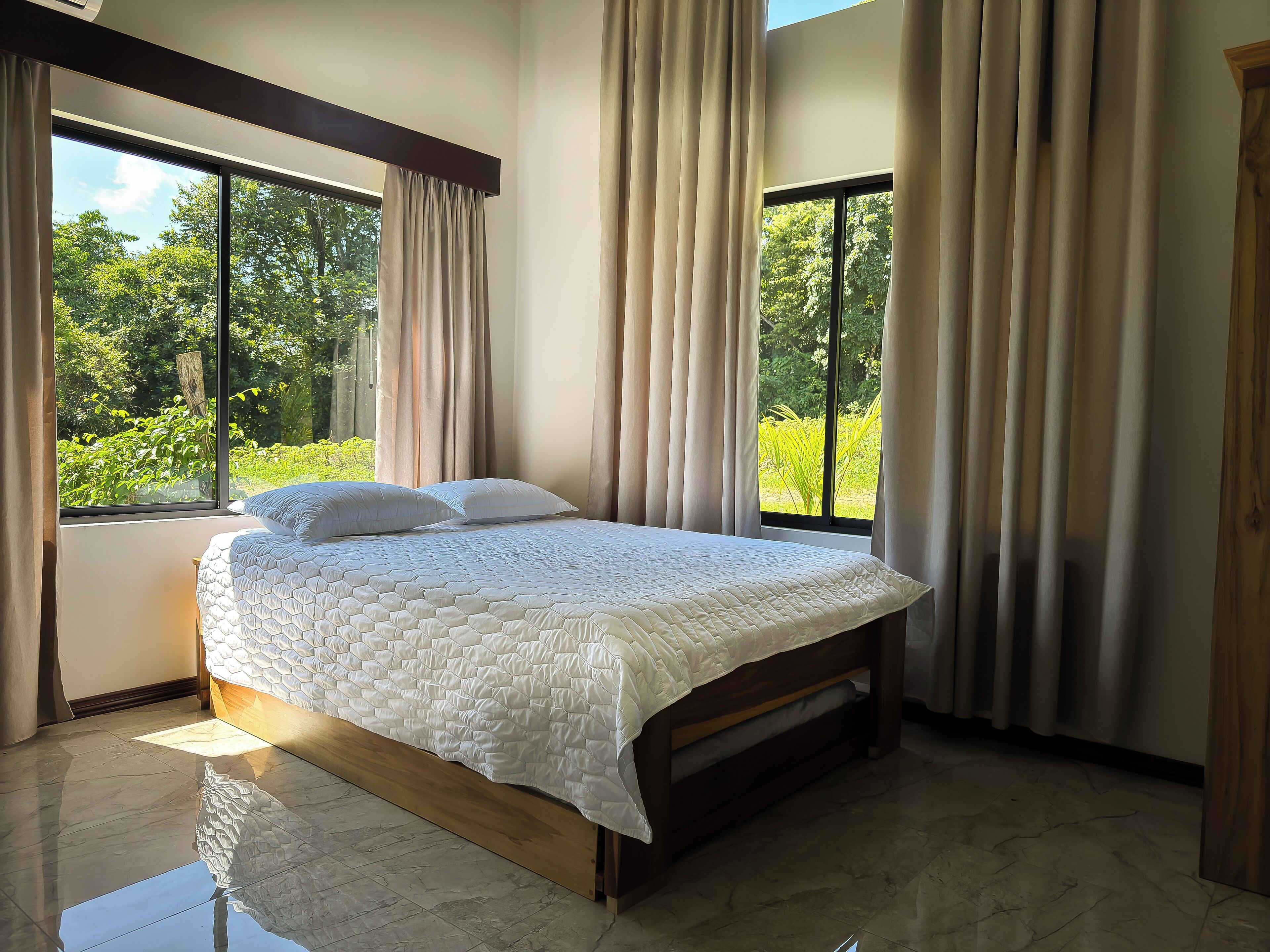 Un dormitorio con una cama grande, dos ventanas y vistas al verde exterior.