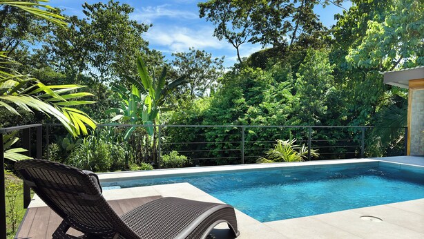 A swimming pool with a wicker lounge chair in the foreground, surrounded by lush greenery. - Oro Verde Lodge (Peñas Blancas)