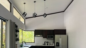 A modern kitchen with a central island, bar stools, and a large window providing natural light. - Oro Verde Lodge (Peñas Blancas)