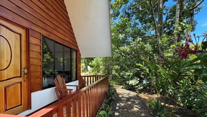 A wooden balcony with a view of a lush garden and a white building. - Oro Verde Lodge (Peñas Blancas)