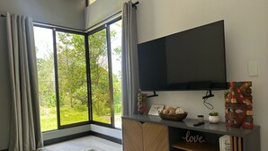 A modern living room with a large TV, a wooden cabinet, and a view of greenery through a sliding glass door. - Oro Verde Lodge (Peñas Blancas)