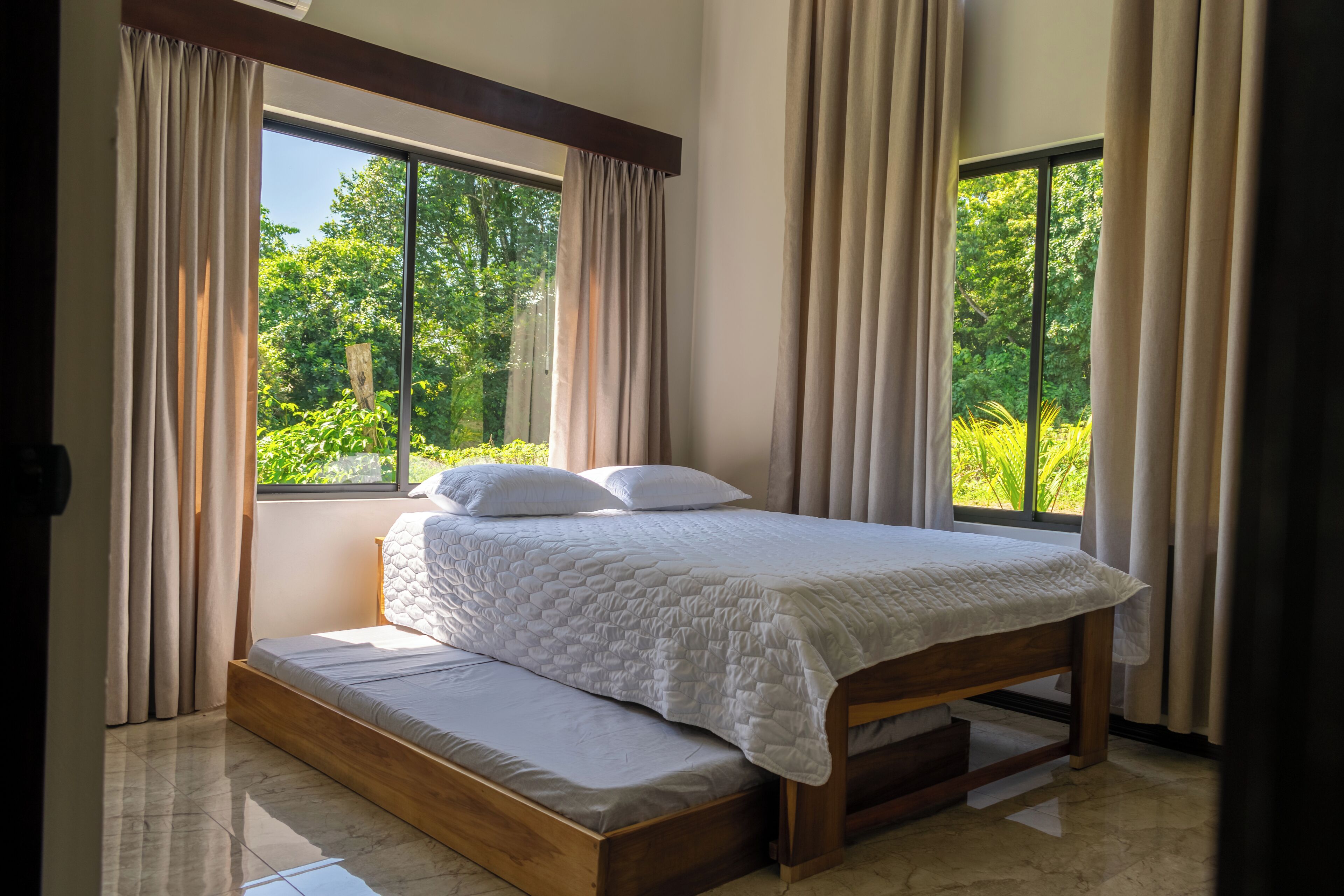 Un dormitorio con cama, cortinas y ventanas amplias.