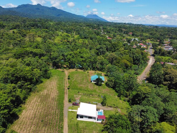 Vista aérea de una zona rural con un campo grande, una casa con techo rojo y una montaña al fondo.