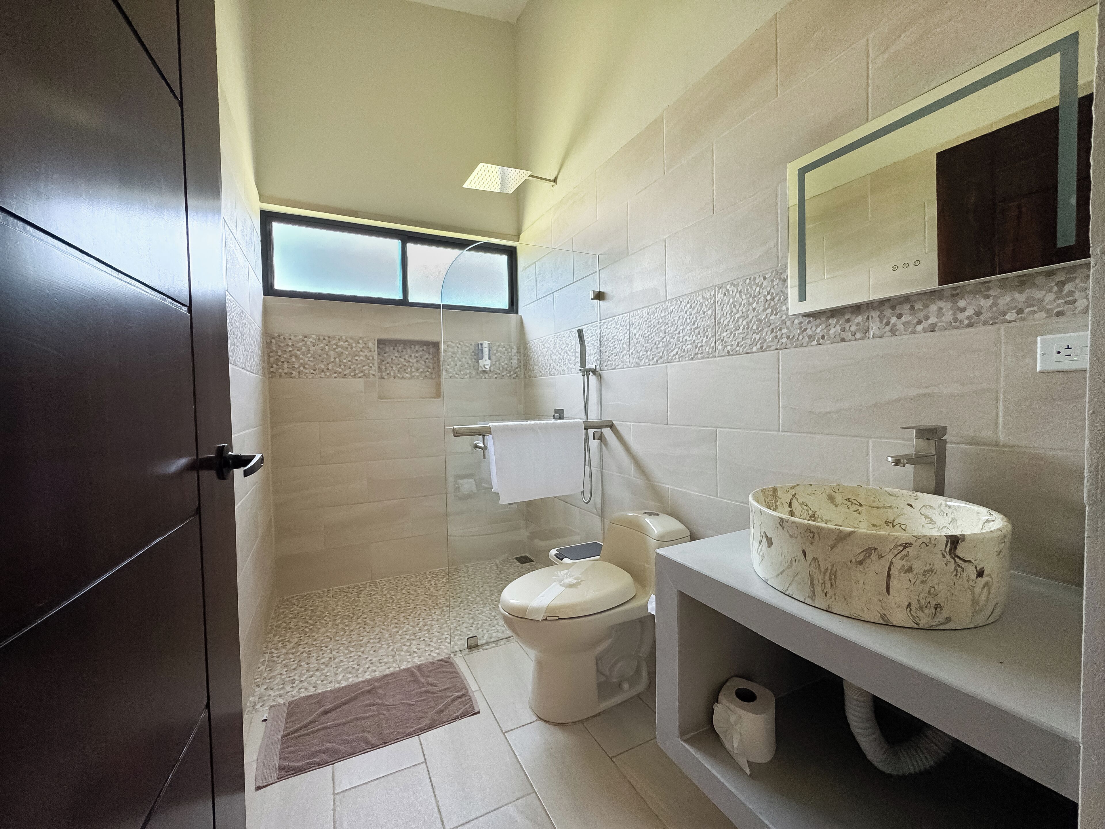 Un baño moderno con cabina de ducha de vidrio, inodoro y tocador con lavamanos de mármol.