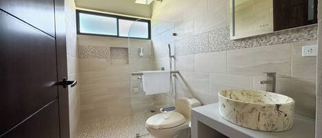 Un baño moderno con cabina de ducha de vidrio, inodoro y tocador con lavamanos de mármol.