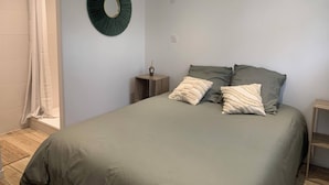 Une chambre à coucher avec un lit, des oreillers, une table de chevet, un miroir fixé au mur et un rideau de douche.