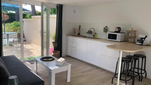 Une cuisine moderne avec des meubles blancs, un four à micro-ondes et une machine à café. On y trouve un petit coin repas avec une table et des chaises, ainsi qu'une porte-fenêtre coulissante donnant sur une terrasse.