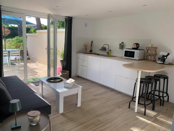 A modern kitchen with white cabinets, a microwave, and a coffee machine. There is a small dining area with a table and chairs, and a sliding glass door leading to a patio.