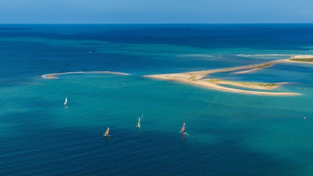 Une vue aérienne d’une zone côtière, avec des eaux bleues et limpides, des plages de sable et de petites îles.