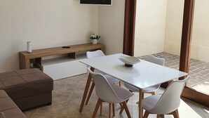 Una sala de estar moderna con una mesa blanca, cuatro sillas, un sofá marrón, un televisor de pantalla plana y un mueble de televisión de madera.