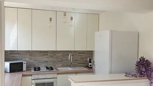 Una cocina compacta con armarios blancos, microondas, estufa, lavamanos y refrigerador.