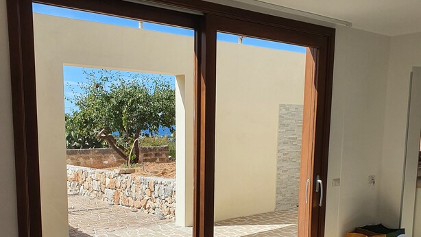 Comedor con una mesa y sillas, proyector en el techo y vista a un patio exterior con un árbol y pared de piedra.