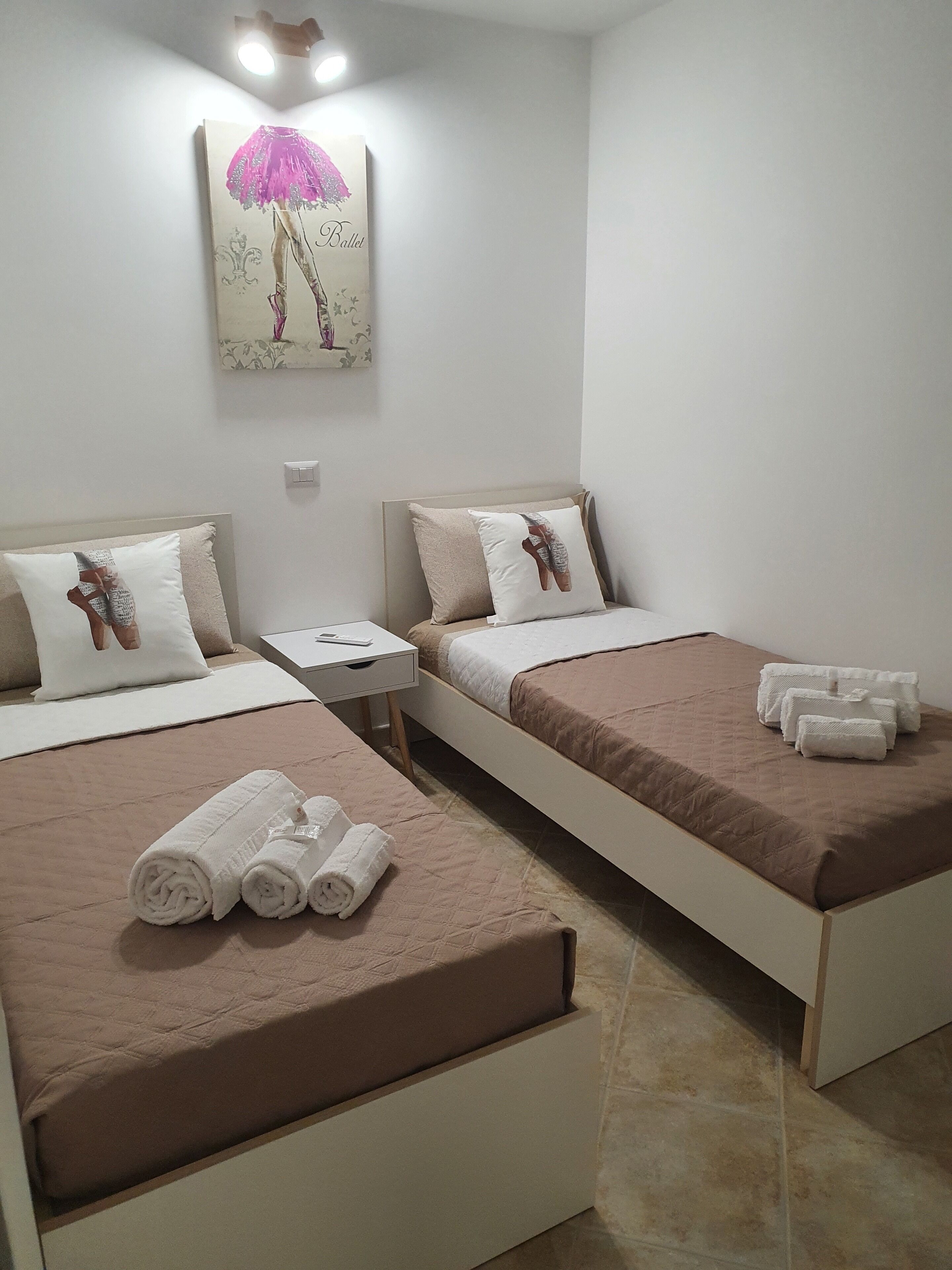 A hotel room with two beds, each with a pillow and a blanket. There are towels on the beds and a painting on the wall.
