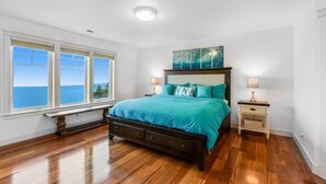 A bedroom with a large bed, a nightstand, a window with a view of the ocean, and a ceiling light. - Custom estate with 6 bedrooms, 4+baths, private beach in enchanting Coupeville. (Coupeville)