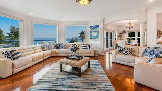 A spacious living room with a large L-shaped sofa, a coffee table, and a view of the ocean. - Custom estate with 6 bedrooms, 4+baths, private beach in enchanting Coupeville. (Coupeville)