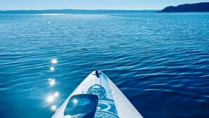 A surfboard on calm water with a distant shoreline and clear sky. - Custom estate with 6 bedrooms, 4+baths, private beach in enchanting Coupeville. (Coupeville)