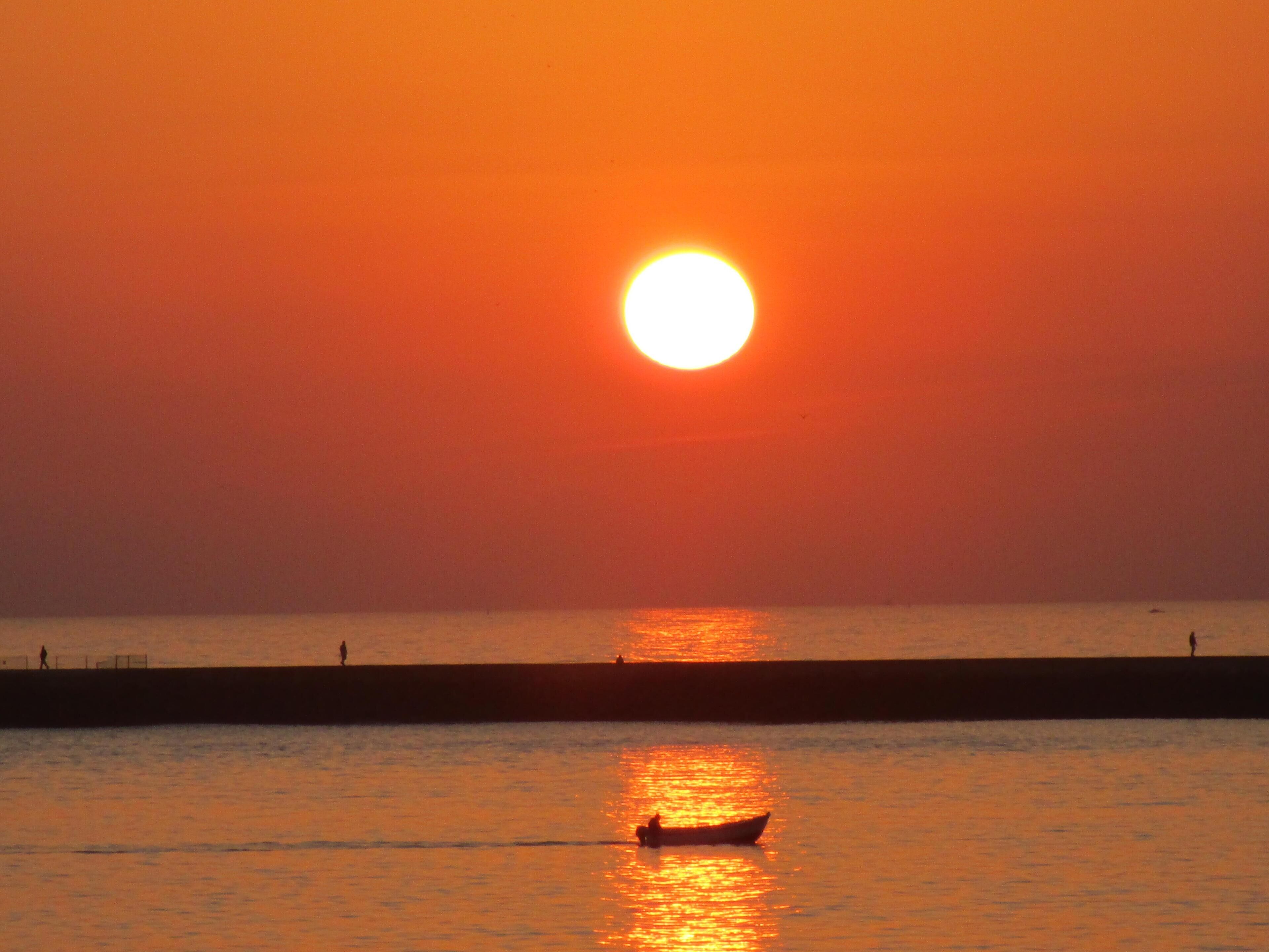 Un coucher de soleil sur une étendue d’eau calme, avec un bateau et une jetée.
