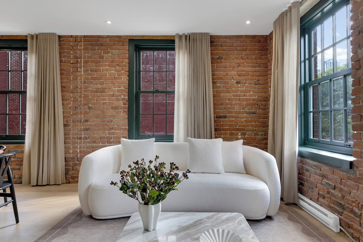 Ein modernes Wohnzimmer mit Backsteinwand, einem weißen Sofa und einer Blumenvase.