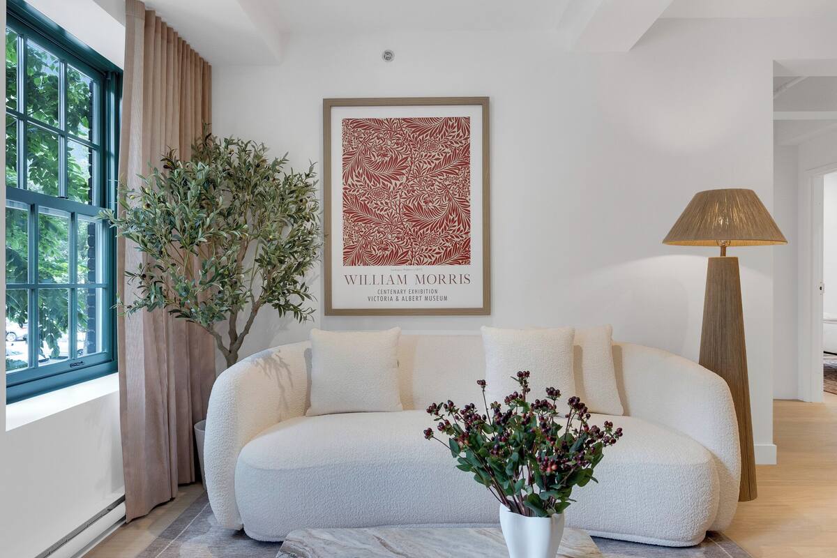 Ein modernes Wohnzimmer mit einem weißen Sofa, einem gerahmten Kunstwerk, einer stehenden Stehlampe und einem Blumentopf.